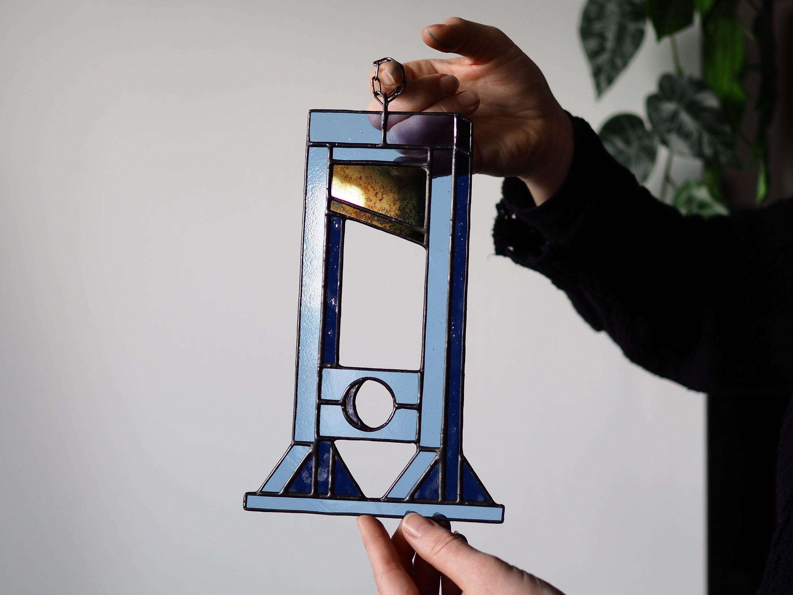 Person holding a stained glass guillotine design against a plain background